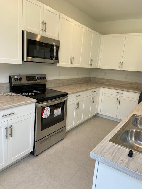 kitchen featuring stainless steel appliances, white cabinetry, and sink