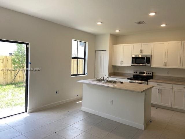 kitchen with white cabinetry, appliances with stainless steel finishes, a wealth of natural light, and an island with sink