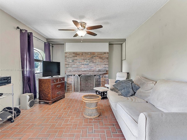 living room with brick wall, a brick fireplace, ceiling fan, and a textured ceiling