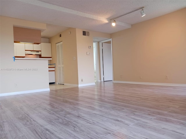 unfurnished living room with a textured ceiling, rail lighting, and light wood-type flooring