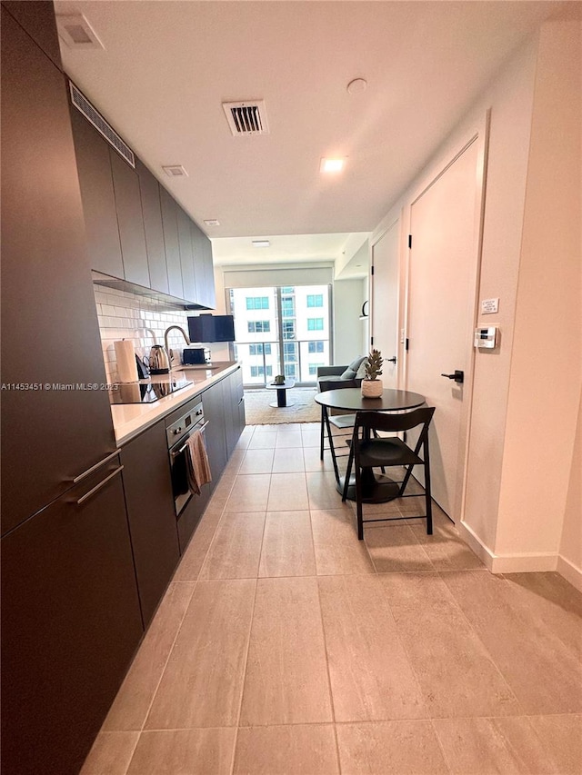 kitchen featuring light tile flooring, backsplash, oven, and sink