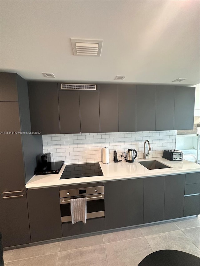 kitchen featuring backsplash, light tile flooring, black electric cooktop, sink, and stainless steel oven