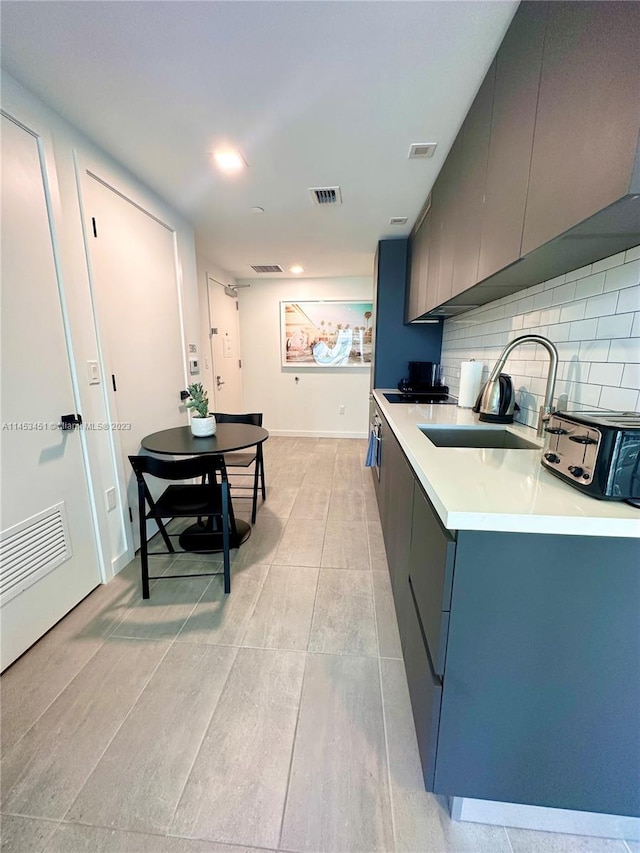 kitchen with gray cabinetry, tasteful backsplash, light tile floors, and sink