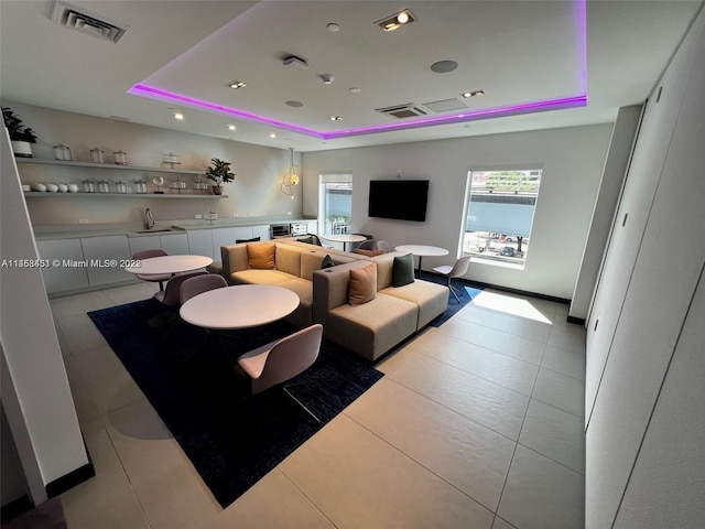 living room with a raised ceiling, light tile flooring, and sink