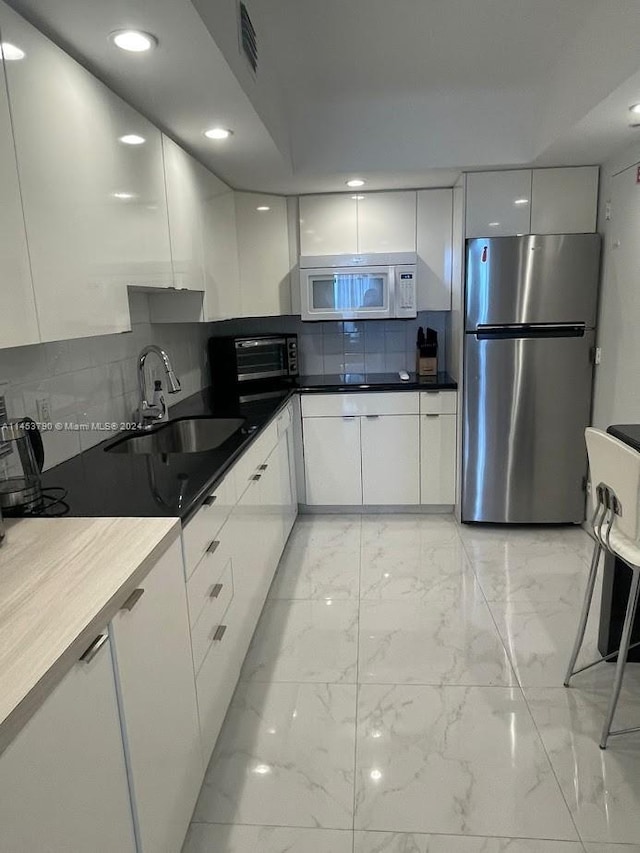 kitchen with stainless steel refrigerator, white cabinetry, backsplash, sink, and light tile flooring