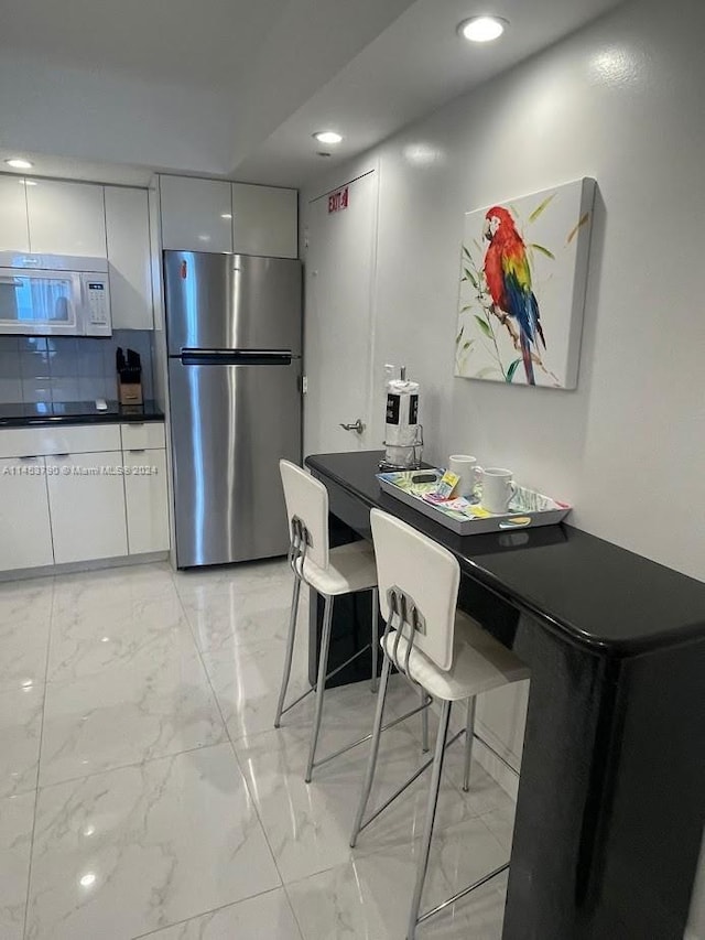 kitchen with stovetop, white cabinets, stainless steel fridge, light tile flooring, and a kitchen bar