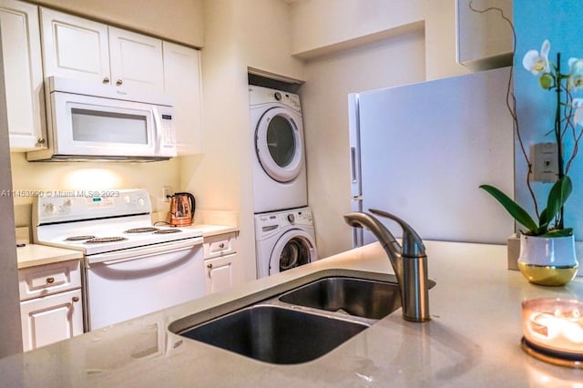 kitchen with sink, white appliances, white cabinetry, and stacked washer and dryer