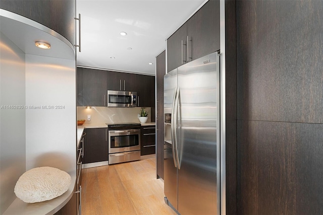 kitchen with appliances with stainless steel finishes, dark brown cabinets, light hardwood / wood-style flooring, and tasteful backsplash