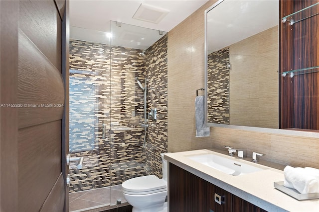 bathroom with a tile shower, vanity with extensive cabinet space, tile walls, and toilet