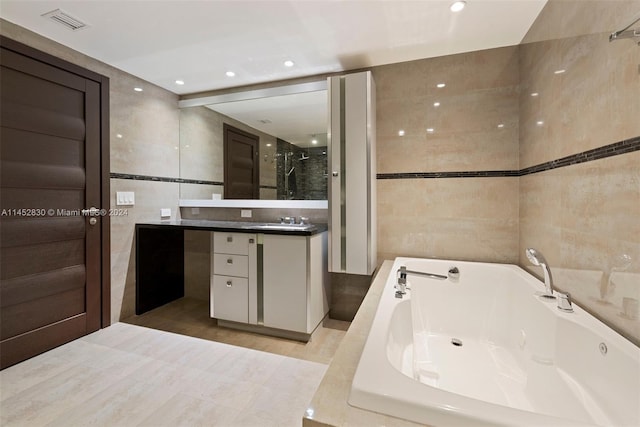 bathroom with tile floors, tiled bath, vanity, and tile walls