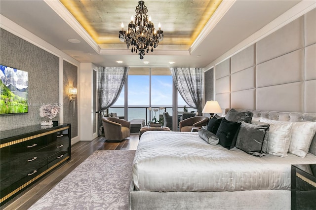 bedroom featuring expansive windows, a tray ceiling, dark hardwood / wood-style floors, an inviting chandelier, and a water view