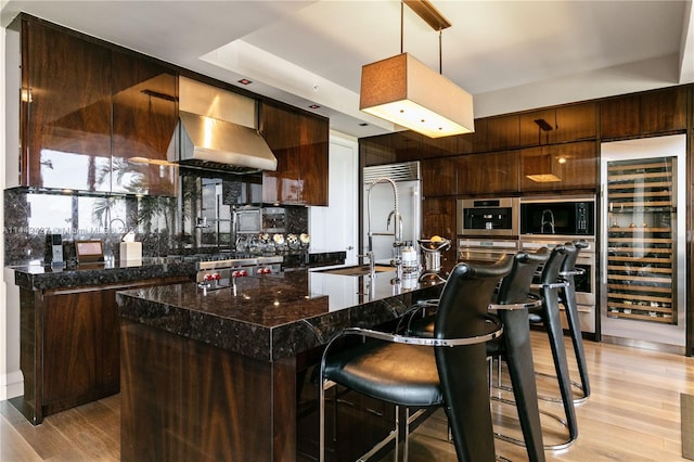 kitchen featuring a center island, beverage cooler, a kitchen bar, light hardwood / wood-style flooring, and wall chimney exhaust hood