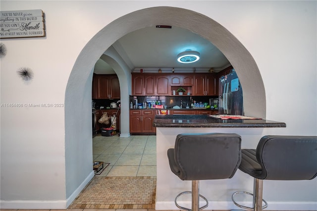 kitchen featuring backsplash, light tile floors, a breakfast bar area, and refrigerator