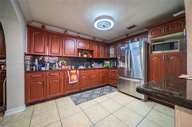 kitchen with light tile flooring, appliances with stainless steel finishes, crown molding, backsplash, and dark stone countertops