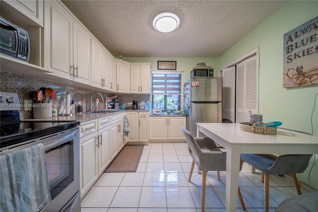 kitchen featuring white cabinetry, light tile flooring, sink, stainless steel appliances, and a textured ceiling