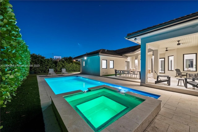 pool at night featuring a patio and an in ground hot tub