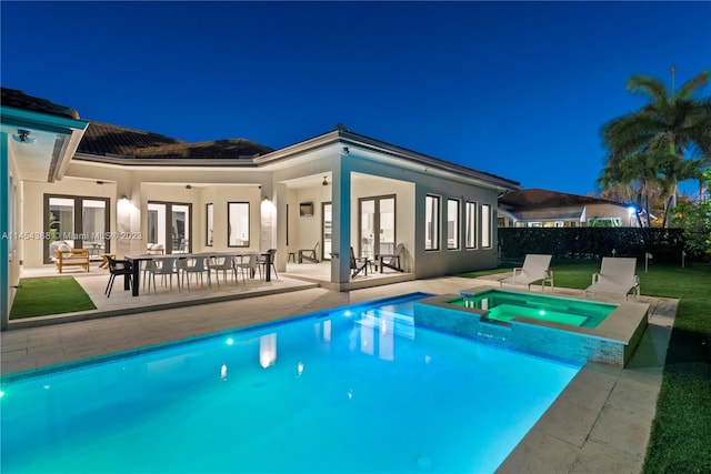 pool at night with a patio area and an in ground hot tub