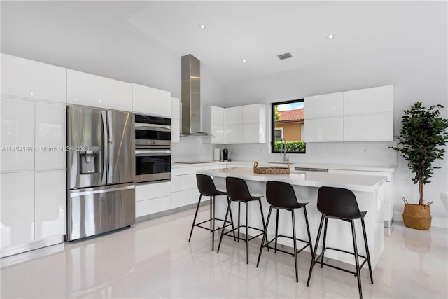 kitchen with white cabinetry, stainless steel appliances, light tile floors, a center island, and wall chimney range hood