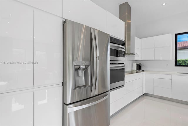 kitchen featuring white cabinets, appliances with stainless steel finishes, light tile floors, and wall chimney range hood