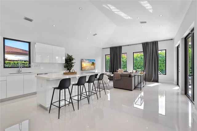 interior space with white cabinetry, sink, light tile floors, a center island, and a breakfast bar area