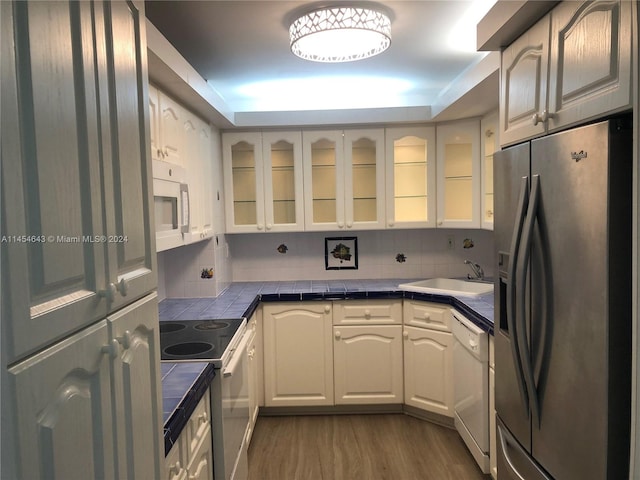 kitchen featuring white appliances, tile countertops, sink, hardwood / wood-style flooring, and white cabinets