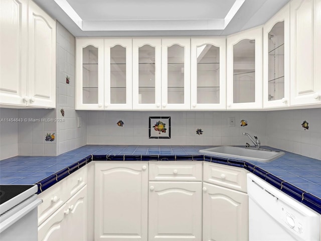 kitchen with white cabinets, white dishwasher, tile counters, and sink