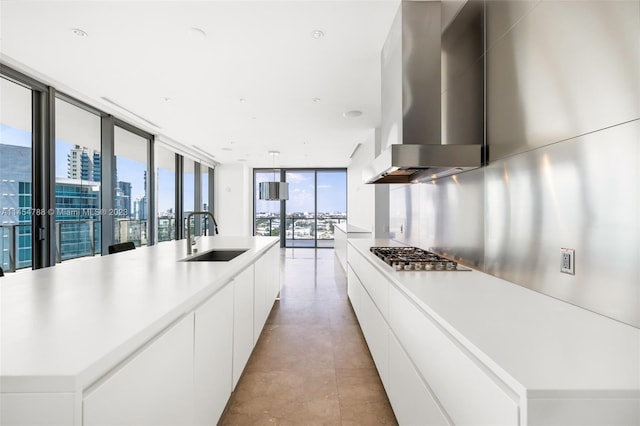 kitchen featuring an island with sink, stainless steel gas cooktop, sink, and wall chimney range hood