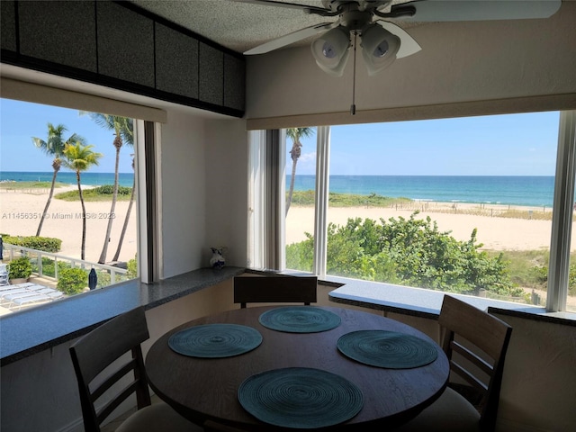 dining space with a water view, a view of the beach, and ceiling fan