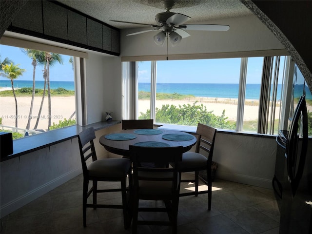 dining room with a water view, a beach view, ceiling fan, and dark tile flooring