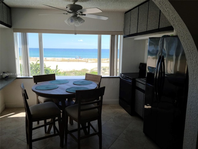 tiled dining space with a water view, ceiling fan, and a textured ceiling