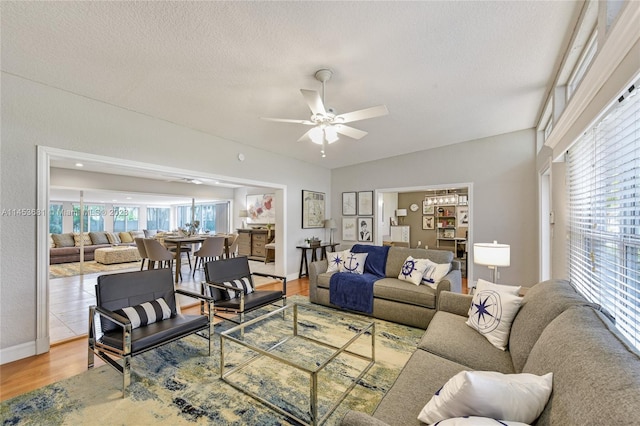 living room with a textured ceiling, ceiling fan, and light wood-type flooring