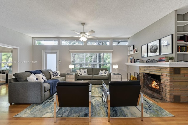 living room with a healthy amount of sunlight, a brick fireplace, ceiling fan, and light wood-type flooring