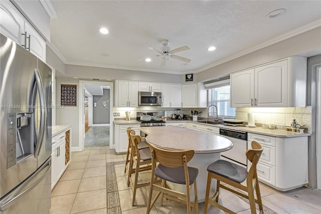 kitchen featuring appliances with stainless steel finishes, white cabinetry, ceiling fan, and a kitchen bar