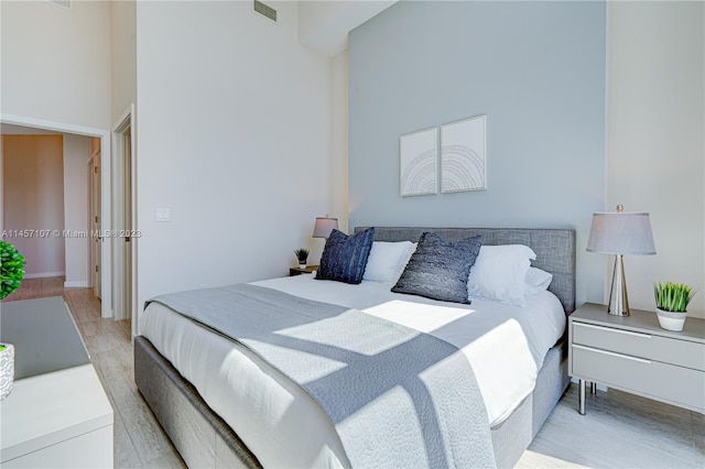 bedroom with light hardwood / wood-style flooring and a towering ceiling