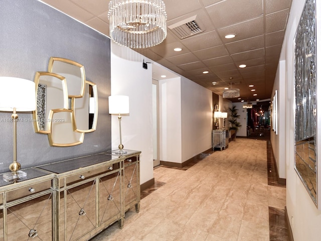 corridor featuring light tile floors, a chandelier, and a drop ceiling