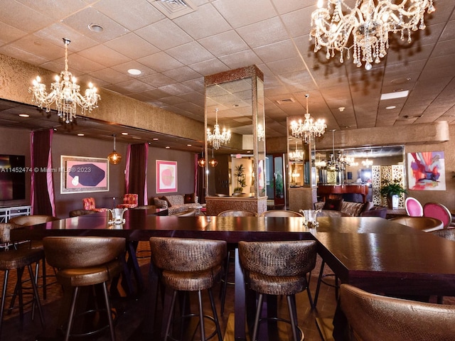 bar featuring decorative light fixtures, a notable chandelier, and a drop ceiling