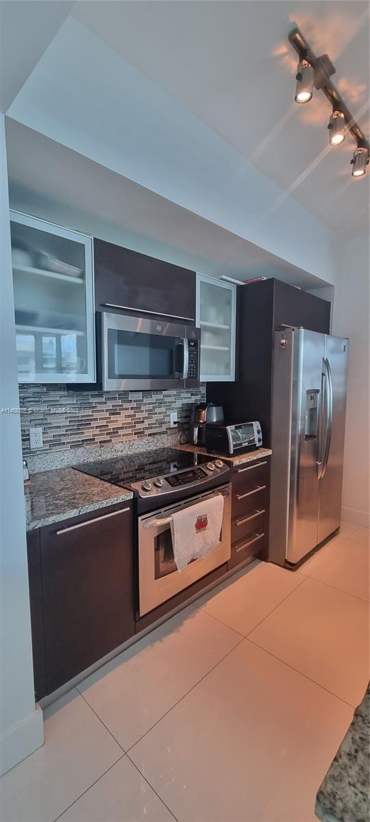 kitchen featuring light tile flooring, rail lighting, stone counters, appliances with stainless steel finishes, and backsplash