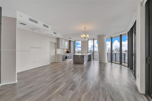 unfurnished living room featuring a notable chandelier, expansive windows, and light wood-type flooring