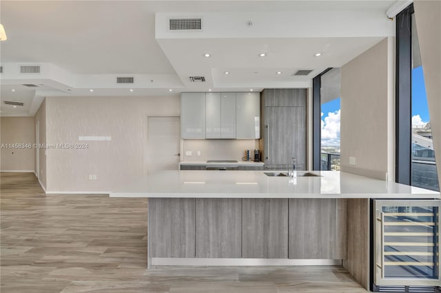 kitchen with sink, floor to ceiling windows, light hardwood / wood-style floors, a center island with sink, and beverage cooler