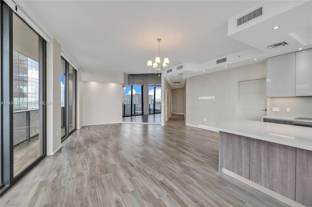 kitchen featuring an inviting chandelier, white cabinets, light wood-type flooring, and a wall of windows