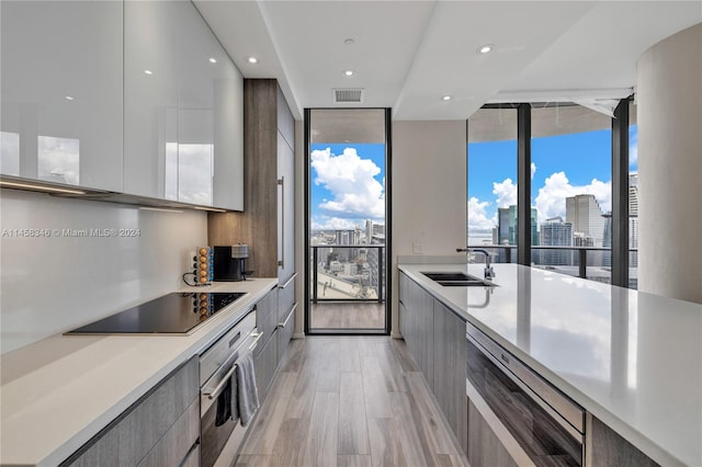 kitchen featuring sink, floor to ceiling windows, dishwashing machine, black electric stovetop, and stainless steel oven