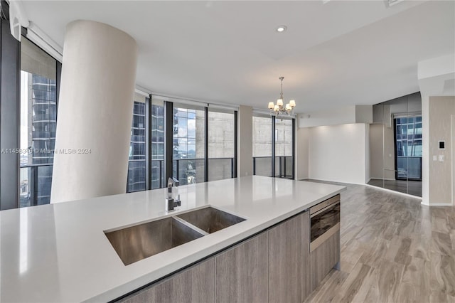 kitchen featuring a wall of windows, sink, a chandelier, decorative light fixtures, and light wood-type flooring