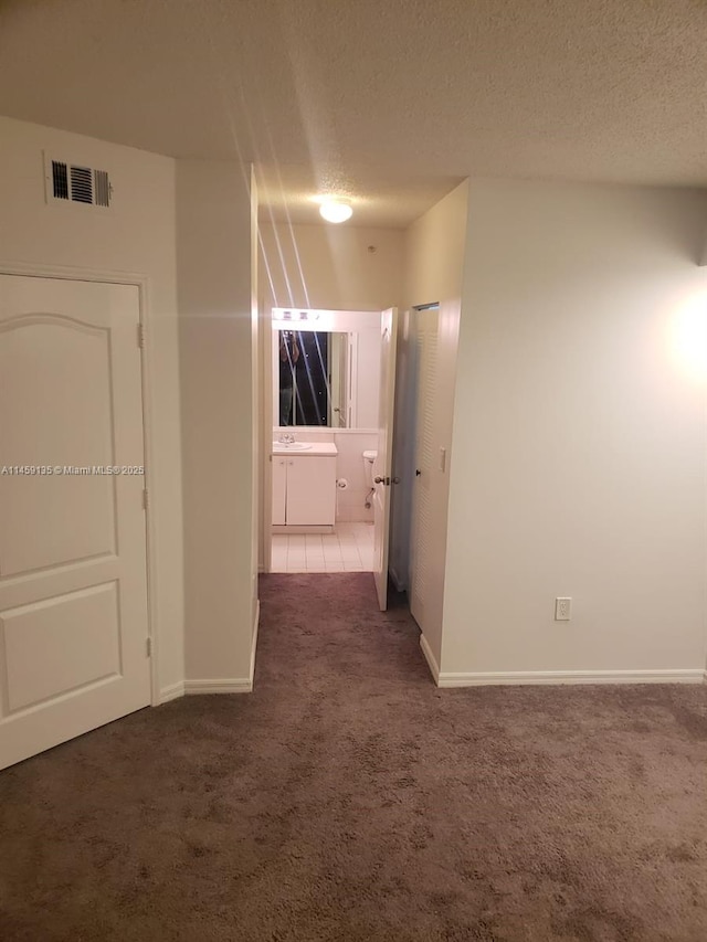 corridor with dark colored carpet and a textured ceiling