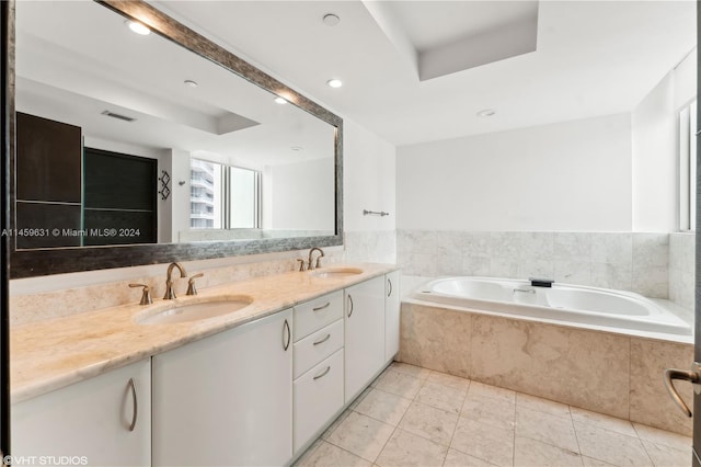 bathroom with a relaxing tiled tub, vanity, and tile patterned floors