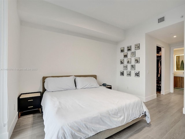 bedroom with a closet, a walk in closet, light hardwood / wood-style flooring, and connected bathroom