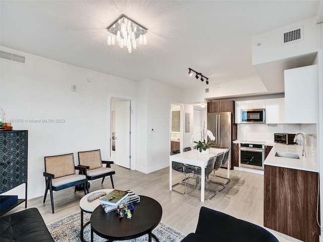 living room featuring track lighting, sink, a chandelier, and light hardwood / wood-style flooring