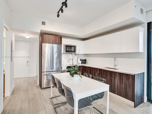 kitchen featuring white cabinetry, a breakfast bar, light hardwood / wood-style flooring, stainless steel appliances, and rail lighting