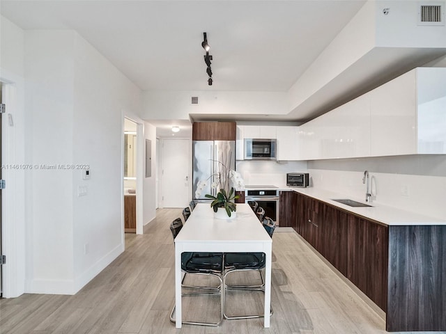 kitchen with sink, dark brown cabinets, appliances with stainless steel finishes, light hardwood / wood-style flooring, and track lighting