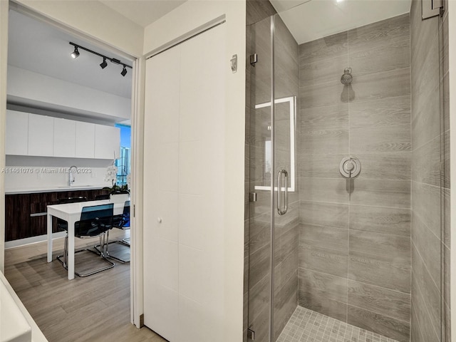 bathroom featuring walk in shower, rail lighting, hardwood / wood-style floors, and sink