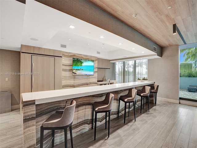 kitchen with light wood-type flooring, wooden ceiling, and a breakfast bar